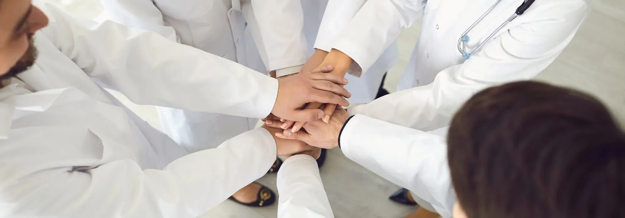 Group of medical professionals in white lab coats standing in a circle with their hands stacked together